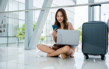 Photo for A happy woman sitting on the airport floor, balancing work and vacation with her laptop and suitcase. Shes a multitasking entrepreneur, making the most of her time. Organization is her ethic. - Royalty Free Image