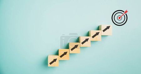 Photo for Target icon positioned on wooden blocks with upward arrows, depicting the progress. Blue background signifies business growth, while conveying concepts of profit, investment, and economic improvement. - Royalty Free Image