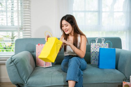 Foto de Happy Asian young woman with many shopping bags at home in living room after long day shopping, Excited female online shopping sitting on couch, Shopper or shopaholic concept - Imagen libre de derechos