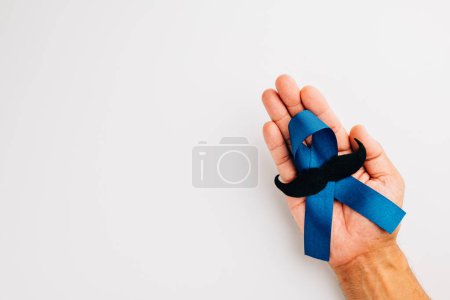 Téléchargez les photos : En novembre, montrez votre soutien à la santé masculine et à la sensibilisation au cancer de la prostate. Les mains tiennent un ruban bleu clair avec une moustache sur un fond bleu un symbole d'unité. - en image libre de droit