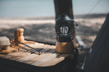 Foto de Una linterna de queroseno antiguo y una lámpara de camping led brillante en una mesa de madera en la playa. Perfecto para camping de verano y viajes al aire libre. Viejo se encuentra nuevo en el aire libre. - Imagen libre de derechos