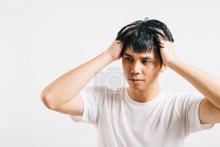 Photo for Portrait of a young Asian man with a sad and tired face, holding his head in despair due to stress and a severe headache. Studio shot isolated on white, symbolizing his distress. - Royalty Free Image