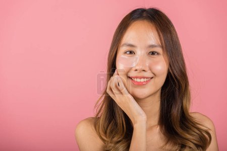 Photo for Anti aging. Asian beautiful young woman smiling mask cosmetic patches gel under the eyes, Portrait female applying medical hydrogel eye patch on face, studio shot isolated on pink background, skincare - Royalty Free Image