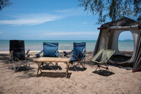 Foto de Sillas, mesa de picnic y tienda de campaña en la playa, una escena matutina para acampar en familia y relajarse al aire libre. Abraza el mar, la naturaleza y la alegría de un nuevo viaje. El medio ambiente es tu lienzo. - Imagen libre de derechos