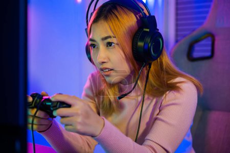 Téléchargez les photos : You win. Gamer using joystick controller plays online video game with computer neon lights she winning, woman wear gaming headphones playing live stream esports games console at home celebrating win - en image libre de droit