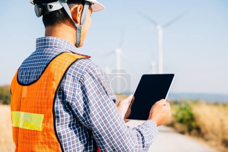Photo for An engineer tablet in hand works at windmill farm. Generating clean energy the technicians expertise guarantees turbine efficiency. Global innovation in electricity control a confident stance. - Royalty Free Image