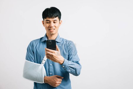 Photo for A man confidently smiles with a broken arm, using a splint, and holding a smartphone. An upbeat Asian woman with a sling-supported hand, isolated on white. Social media and copy space. - Royalty Free Image
