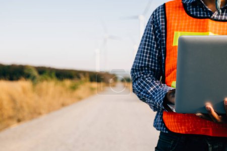 Photo for Engineer holding laptop at wind turbines ensuring efficiency. Service technician focuses on turbine performance. Landscape development innovated for windmill service and quality assurance. - Royalty Free Image