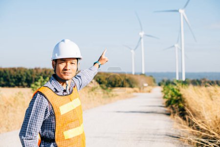 Téléchargez les photos : Technicien ingénieur vêtu de casque au parc éolien. Garantir une énergie propre un expert asiatique vérifie l'efficacité de la turbine. Innover pour la sécurité électrique mondiale dévouement et expertise dépeints. - en image libre de droit