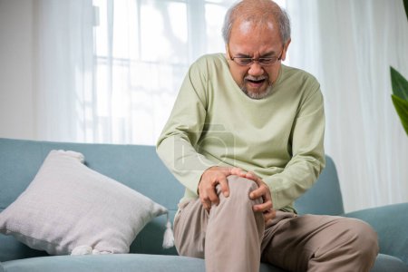 Photo for Old age. Asian senior man retirement knee joint pain on sofa, Elderly old man sitting down hands hold knee, Grandfather people health care bone problem at home - Royalty Free Image