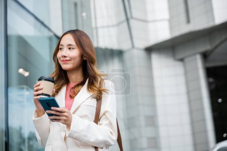 Foto de Productiva mujer de negocios, multitarea con una taza de café caliente y un teléfono móvil, manteniéndose al tanto de su juego. - Imagen libre de derechos
