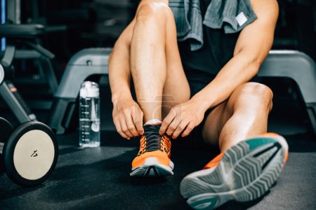 Photo for A close-up of a mans legs tying his shoelaces before a workout. The shot emphasizes the detail of his shoes and the importance of proper footwear in fitness. - Royalty Free Image