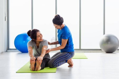 Téléchargez les photos : Asiatique jeune enseignante enseigner à un étudiant adulte faisant du yoga étirement position en studio. Deux femmes enseignant le yoga et le plaisir ensemble, sport féminin fitness concept d'entraînement - en image libre de droit