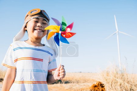 Foto de Infantil participación juguetona cerca de las turbinas eólicas con un juguete molinete celebra la energía eólica. Ilustra la innovación en electricidad limpia en un paisaje de molino de viento rural contra un cielo soleado y claro. - Imagen libre de derechos