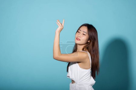 Photo for Asian young woman hand up cover face protect sun light and UV smile in studio shot isolated on blue background, female raising arm and hand in protection and block sunshine, sunscreen cream advertise - Royalty Free Image