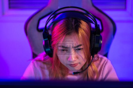 Téléchargez les photos : Happy Gamer endeavor plays online video games tournament with computer neon lights, young woman wearing gaming headphones intend to do playing live stream games online at home - en image libre de droit