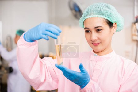 Photo for Within juice beverage factory woman food engineer illustrates food and beverage quality and safety testing using test tubes for sampling basil or chia seeds in bottled products emphasizing expertise - Royalty Free Image