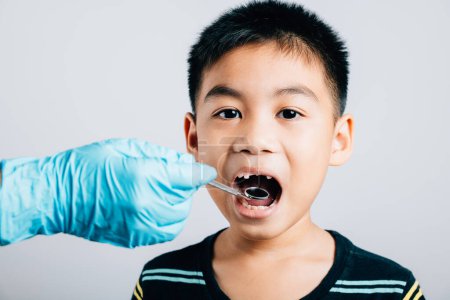 Téléchargez les photos : Le dentiste pédiatrique examine une bouche d'enfant après avoir retiré une dent de lait en vrac. Assistante dentaire aide à l'examen des instruments dentaires. Le médecin utilise un miroir buccal pour vérifier la cavité dentaire - en image libre de droit