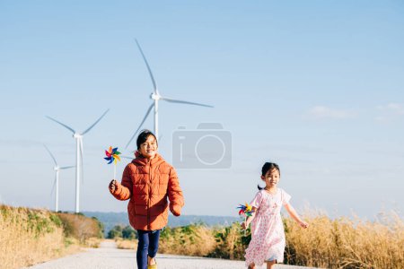 Photo for Two children girl with pinwheel happily near windmills. Family moments at turbines symbolize clean energy. Children joy windmill circle in sky represents sustainable cheerful community. - Royalty Free Image