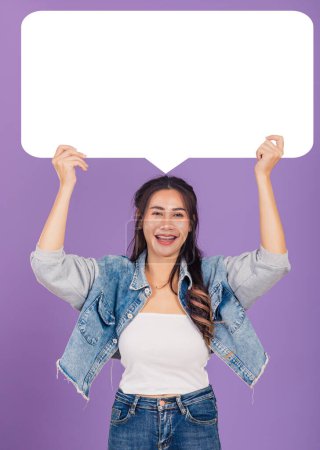 Photo for Happy Asian beautiful young woman smiling excited wear denims hold empty speech bubble sign, Portrait female posing show up for your idea looking at camera, studio shot isolated on purple background - Royalty Free Image