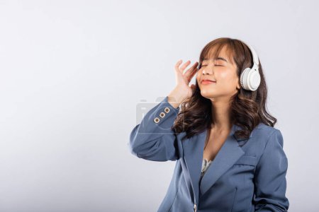 Téléchargez les photos : Femme excitée souriant écouter de la radio de musique dans les écouteurs bluetooth et tenant studio de téléphone tourné fond blanc isolé, heureux asiatique jeune femme écouter la technologie moderne téléphone mobile - en image libre de droit