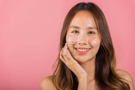 Téléchargez les photos : Eye skin treatment. Asian beautiful young woman smiling mask cosmetic patches gel under the eyes, Portrait female with natural makeup hydrogel eye patch on face, isolated on pink background, skincare - en image libre de droit