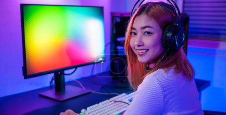 Photo for Smiling young woman wearing gaming headphones intend to do playing live stream games online at home looking to camera, Happy Gamer endeavor plays online video games tournament with computer neon light - Royalty Free Image