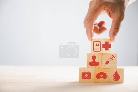 Photo for Conceptual portrayal, Hand clutches wooden block with healthcare and medical icons. Reflecting safety, health, and family well-being. Symbolic of pharmacy, heart care, and happiness. - Royalty Free Image