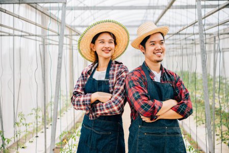 Photo for Happiness blooms in tomato hydroponic farm with Asian couple. Smiling farmers crossed arms carrying quality vegetables. Portrait of successful husband and wife in the greenhouse. Farming joy. - Royalty Free Image