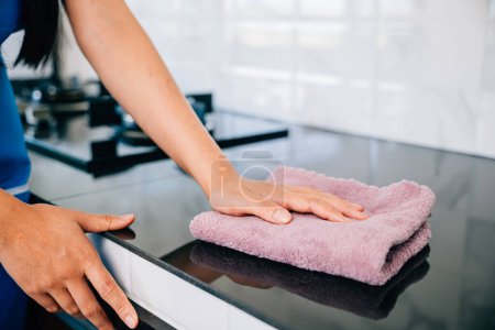 Photo for A cheerful housewife diligently cleans her kitchen table using a rag and detergent, emphasizing safety and hygiene. Illustrating routine household cleaning for cleanliness. Wiping cloth kitchen - Royalty Free Image