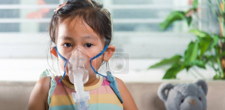 Téléchargez les photos : Kid girl making makes inhalation nebulizer steam sick cough at home, Asian Child using nebulizer mask equipment alone have smoke, stuffy nose and runny, oxygen spray inhaler therapy, Health medical - en image libre de droit