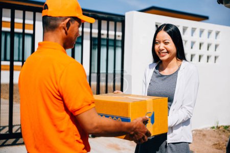 Photo for At the front house door a woman customer receives a cardboard parcel from a smiling delivery service courier man showcasing efficient home delivery logistics and customer satisfaction. - Royalty Free Image