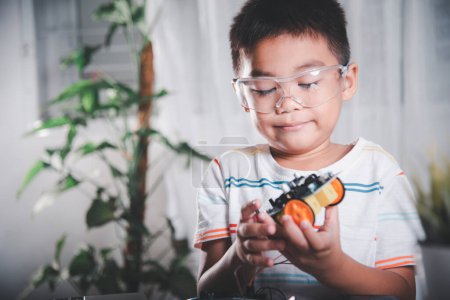 Téléchargez les photos : Petit enfant essayant d'assembler la roue de construction au jouet de voiture, enfant asiatique assemblant la roue dans les devoirs de voiture robot Arduino, créant un atelier de technologie d'IA électronique leçon d'école en ligne - en image libre de droit