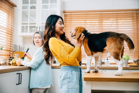 Foto de En la cocina, una mujer asiática mayor, su hija y una mujer joven encuentran alegría jugando con su perro Beagle, haciendo hincapié en la unión, la unión y el disfrute de la propiedad de mascotas. - Imagen libre de derechos