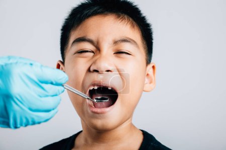 Téléchargez les photos : Chez un dentiste pédiatrique, un médecin examine la bouche d'un enfant après l'extraction d'une dent de lait en vrac. Les instruments dentaires aident à l'examen. Le médecin utilise un miroir buccal pour vérifier la cavité dentaire - en image libre de droit