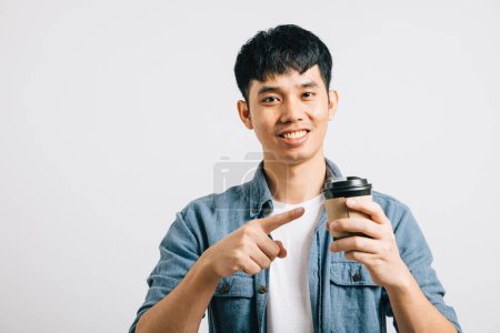 Téléchargez les photos : Portrait d'un adolescent asiatique souriant avec une tasse de café à emporter, pointant vers son idée optimiste. Plan studio isolé sur fond blanc, positivité rayonnante. - en image libre de droit
