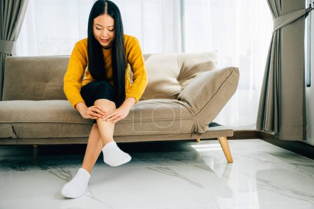 Photo for Highlighting health care concept, woman on sofa holds her injured ankle. Emphasizing varicose vein prevention leg recovery and pain relief for the patient. medical - Royalty Free Image