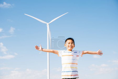 Foto de Un niño alegre disfruta de la belleza de los parques eólicos. La diversión familiar en medio de las turbinas significa un escape lúdico a la naturaleza. La felicidad de los niños rodeados de energía limpia y tecnología de molinos de viento. - Imagen libre de derechos