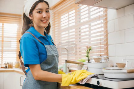 Foto de Mujer asiática con guantes protectores limpia el polvo de la estufa de gas en la cocina. Poner énfasis en la higiene de las manos rutina de limpieza. Limpiador en el trabajo guante de seguridad cuidado de la casa. Limpieza de limpieza concepto de limpieza. - Imagen libre de derechos