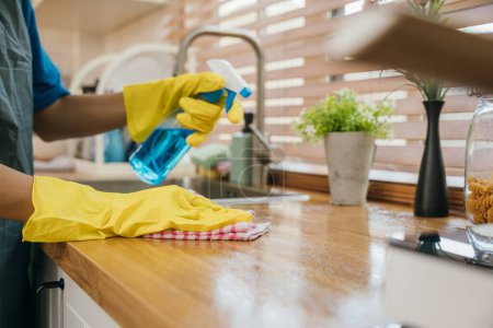 Photo for Occupied woman disinfects kitchen worktop with spray ensuring hygiene. Housekeeping routine for a clean home. Portrait of diligent cleaner caring for home purity. Clean disinfect home care. Give me. - Royalty Free Image