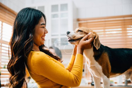 Photo for With her Beagle, an Asian woman embraces the kitchen as a place of happiness and play. Their joyful interaction exemplifies the care, togetherness, and family enjoyment of having a pet. Pet love - Royalty Free Image