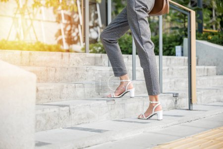 Téléchargez les photos : Femme d'affaires en costume moderne est capturé dans le moment de l'ambition de monter les escaliers de la ville. Son pied noir chaussure symbolise l'effort acharné et le progrès incarnant l'esprit de succès dans le monde des entreprises. - en image libre de droit