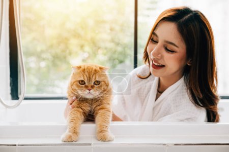 Photo for Bathing bliss, an adult woman smiles while holding her Scottish Fold cat in the bathroom, creating a scene of relaxation and pet adoration. - Royalty Free Image