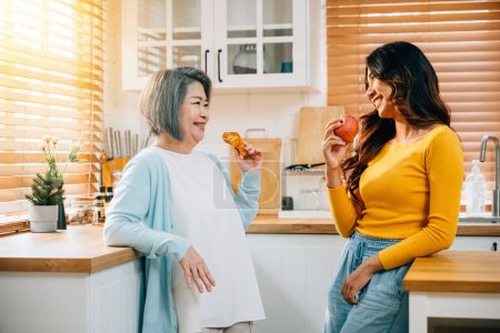 Photo for In the kitchen, an attractive young Asian woman and her mother share a moment of togetherness. Their smiles reflect the happiness and family bonding over food and learning. - Royalty Free Image