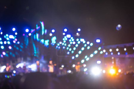 Foto de La noche está llena de música y emoción en un evento principal del festival de conciertos. Una multitud irreconocible vítores se reúne frente al escenario brillantemente iluminado y la llamarada de la lente se suma a la atmósfera animada. - Imagen libre de derechos