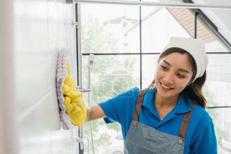 Photo for In a bathroom a maid uses a microfiber cloth to clean ceramic tiles wearing protective gloves. Routine cleaning signifies a commitment to purity and hygiene in commercial services. - Royalty Free Image