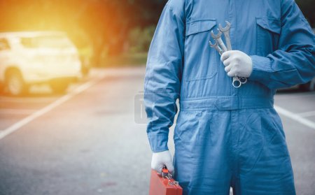 Photo for Skilled car mechanic at work on the road, holding a large wrench with hands clad in blue workwear. Close-up shot of the hands. - Royalty Free Image