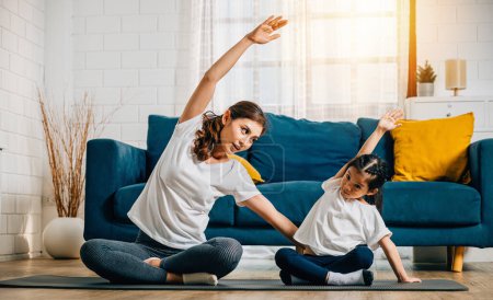 Photo for A mother supports her daughter during family yoga focusing on stretch and balance. Their smiles create a heartwarming and harmonious moment at home. - Royalty Free Image