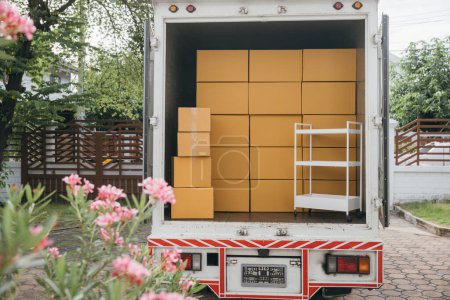 Photo for Outdoors a white delivery van and open car trunk carrying moving cardboard boxes. Logistic service for house relocation. Transporting items in crowded truck. Moving Day Concept. - Royalty Free Image