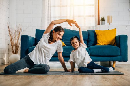 Téléchargez les photos : Une mère entraîne sa petite fille dans le yoga en créant un lien familial rempli de bonheur détente et de convivialité. Leurs sourires reflètent la joie et la vitalité dans leur vie domestique. - en image libre de droit